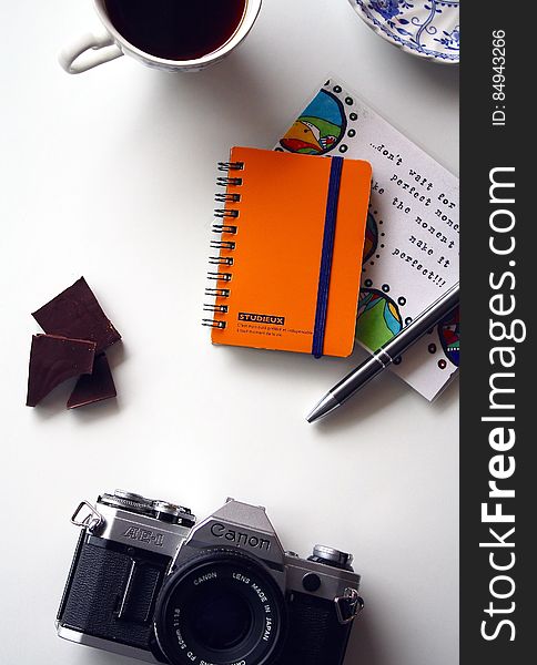 Canon Gray and Black Bridge Camera Near Orange and Blue Spiral Notebook