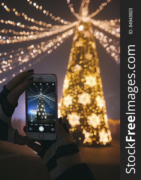 A person photographing a Christmas tree with a smartphone camera. A person photographing a Christmas tree with a smartphone camera.