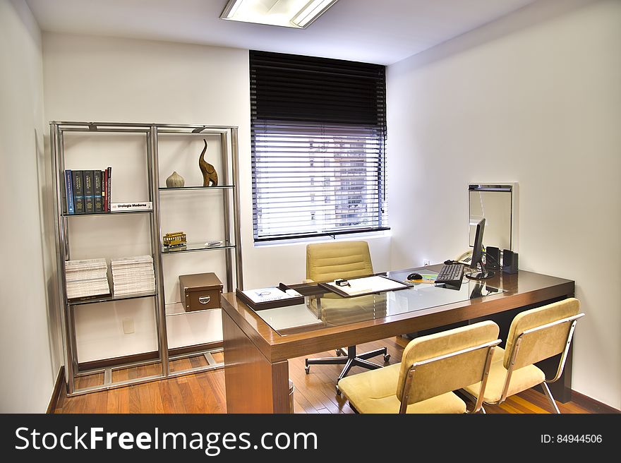 Light, bright office or consulting room with desk and three chairs, window with Venetian blinds and modern bookcase.