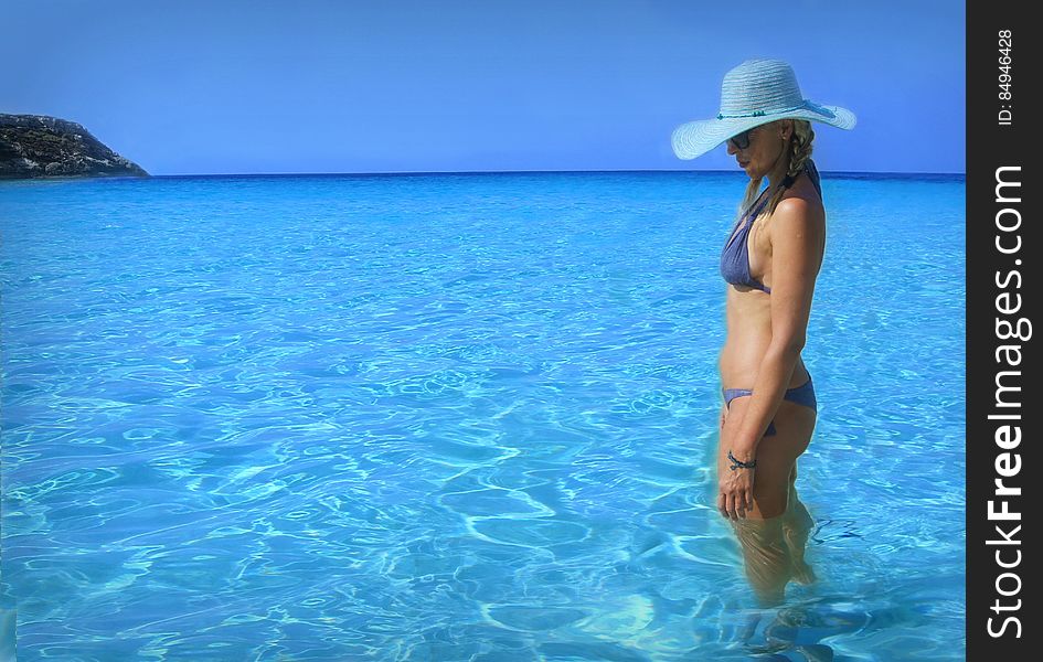 Portrait of woman in bikini with sunhat standing in blue waters on coastline. Portrait of woman in bikini with sunhat standing in blue waters on coastline.