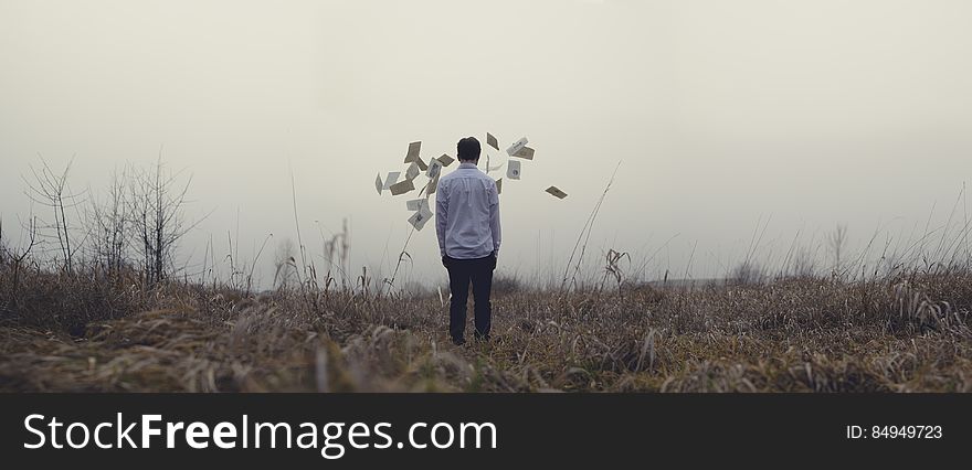 Man Standing In A Field Surrounded By Flying Papers