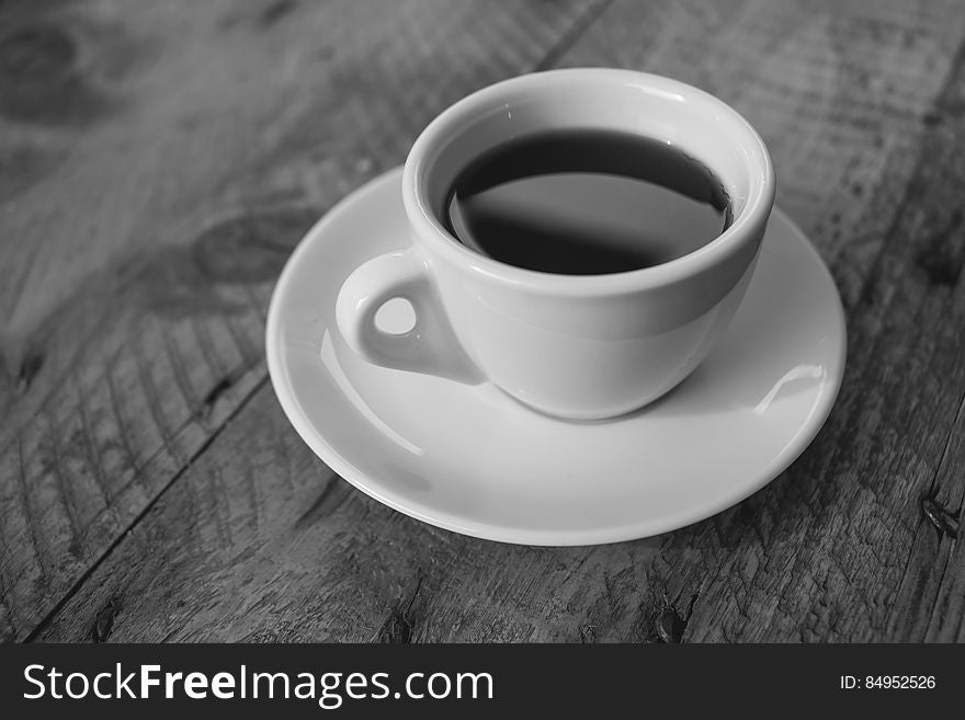 A black and white close up of a cup of coffee on a wooden table.