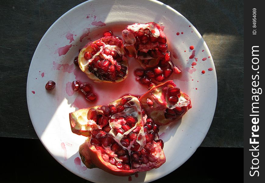 Pomegranate fruit on a white plate open with seeds visible and red spots every where, mainly dark background. Pomegranate fruit on a white plate open with seeds visible and red spots every where, mainly dark background.