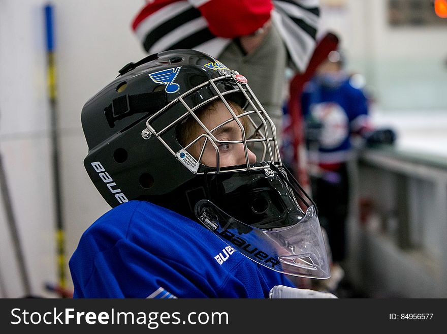 Young hockey player sitting on bench next to rink wearing helmet during match.