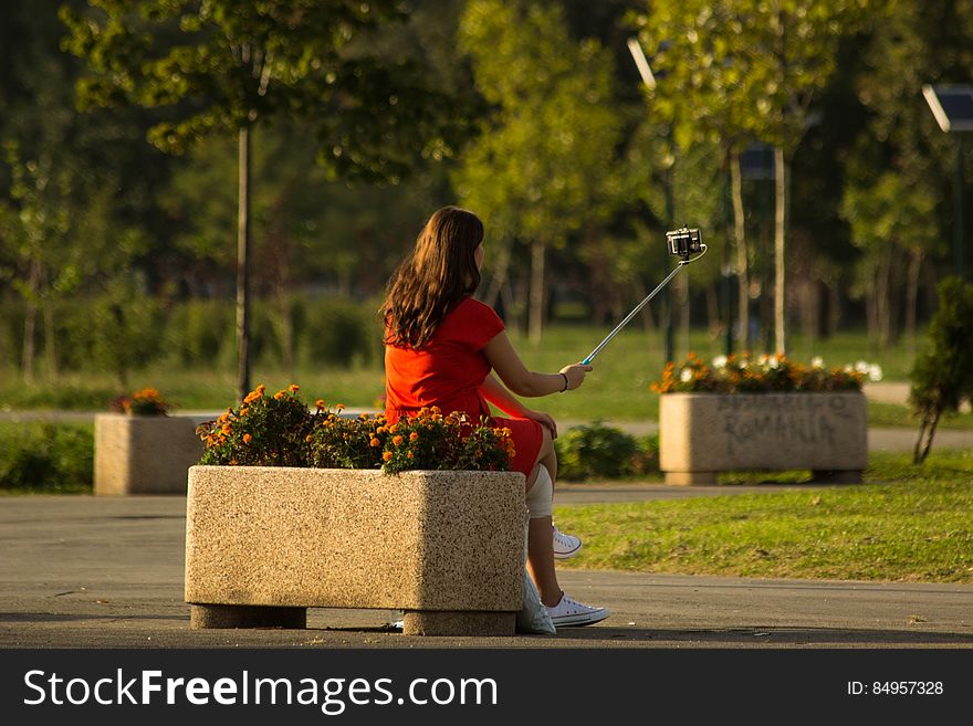 Rear view of girl taking picture with selfie stick in park. Rear view of girl taking picture with selfie stick in park.
