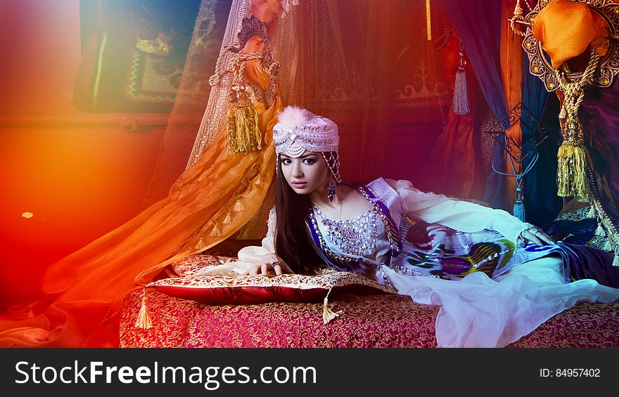 Beautiful young Arabic woman lying on opulent bedroom in traditional clothes with red tone. Beautiful young Arabic woman lying on opulent bedroom in traditional clothes with red tone.