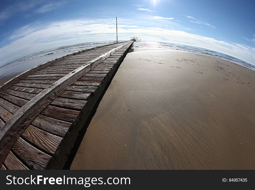 Fish eye view of wooden pier on beach with sea and blue sky in background.