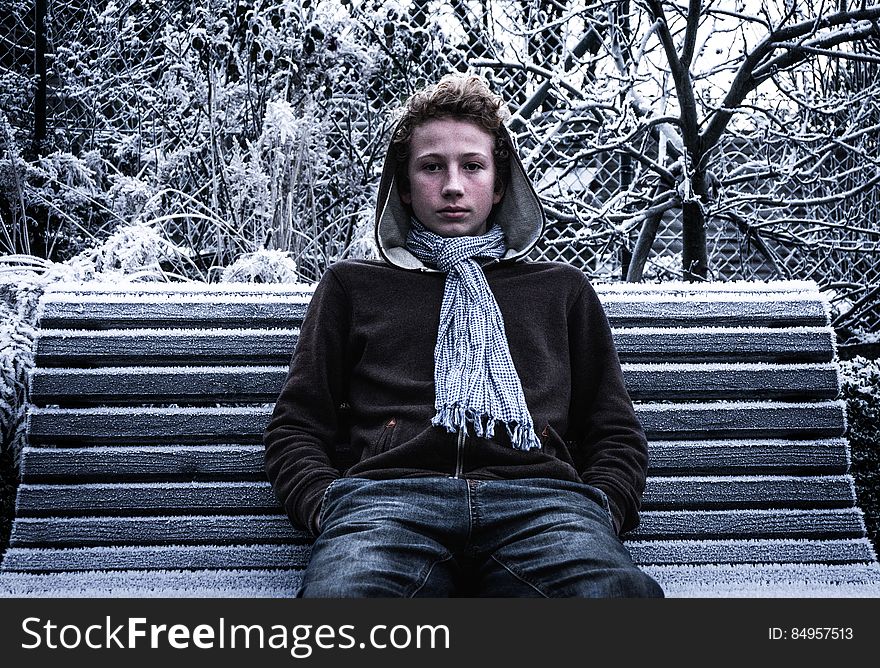Teenager boy sat on park bench wearing hoodie in winter. Teenager boy sat on park bench wearing hoodie in winter.