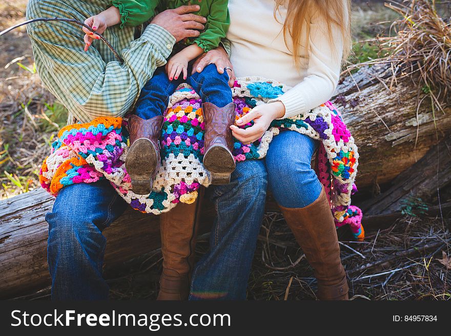 The parents holding a child and sitting outdoors on a log with a colorful quilt. The parents holding a child and sitting outdoors on a log with a colorful quilt.