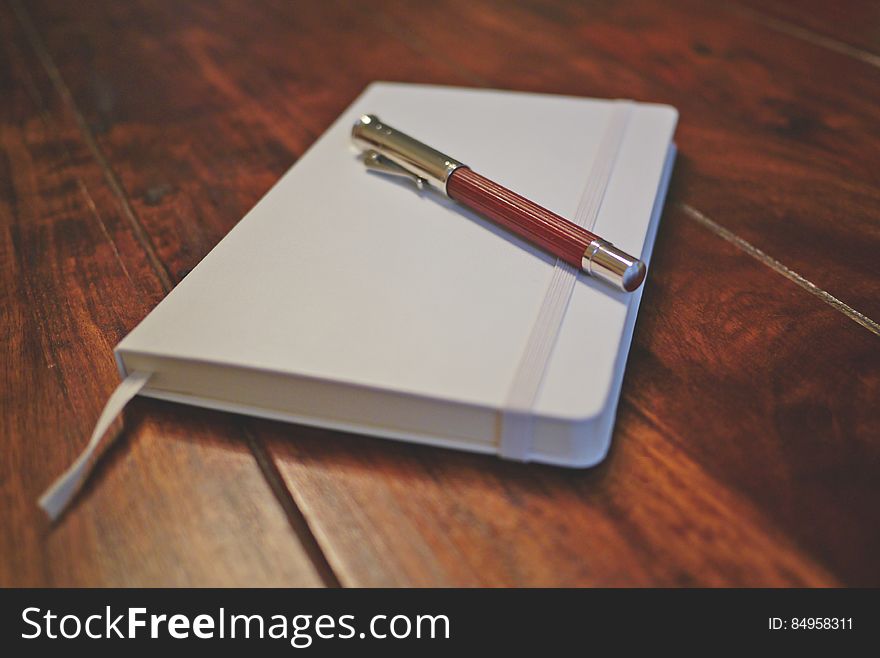 A white notebook and a fountain pen on wooden table. A white notebook and a fountain pen on wooden table.