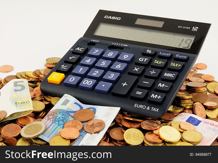 Calculator on pile of Euro coins and banknotes with white background and copy space. Calculator on pile of Euro coins and banknotes with white background and copy space.