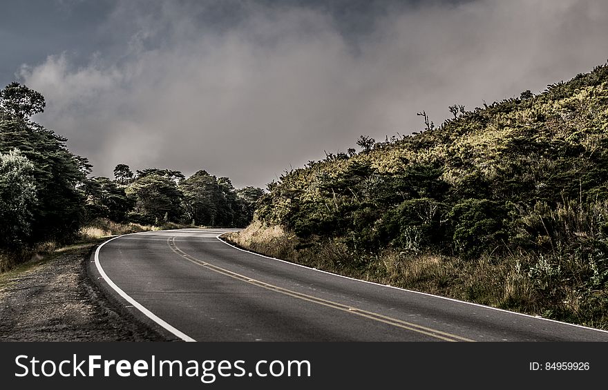 An asphalt road passing through a green hilly landscape.