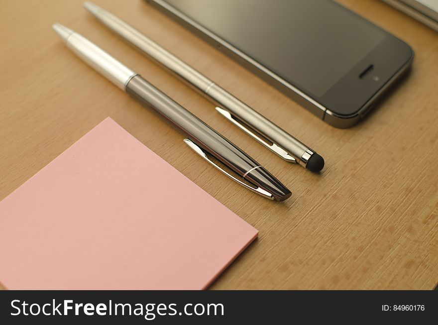 A mobile phone with sticky notes and a pair of pens. A mobile phone with sticky notes and a pair of pens.