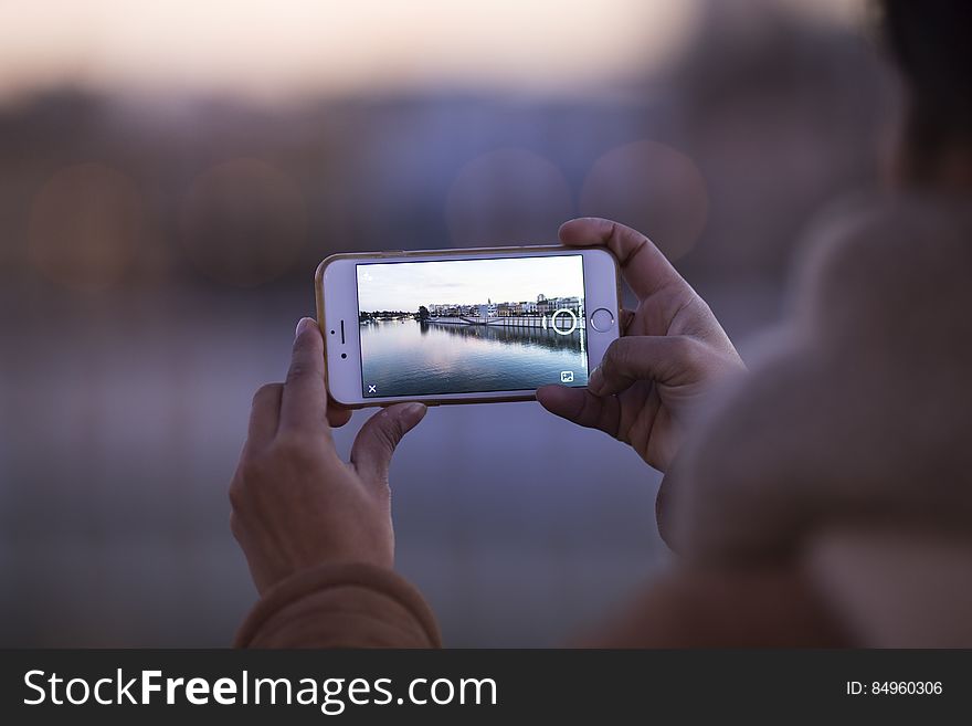A person photographing a river and city view with a smartphone camera. A person photographing a river and city view with a smartphone camera.