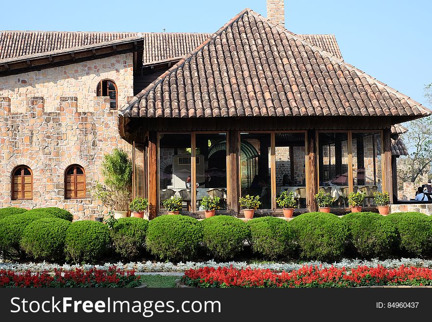 Exterior of a stone rustic building with conservatory, flowers and hedge in foreground.