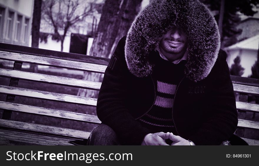 A man wearing a fur-lined jacket sitting on a bench. A man wearing a fur-lined jacket sitting on a bench.