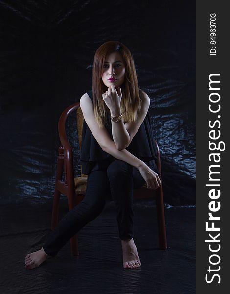 Woman Sitting on Brown Chair With Black Background