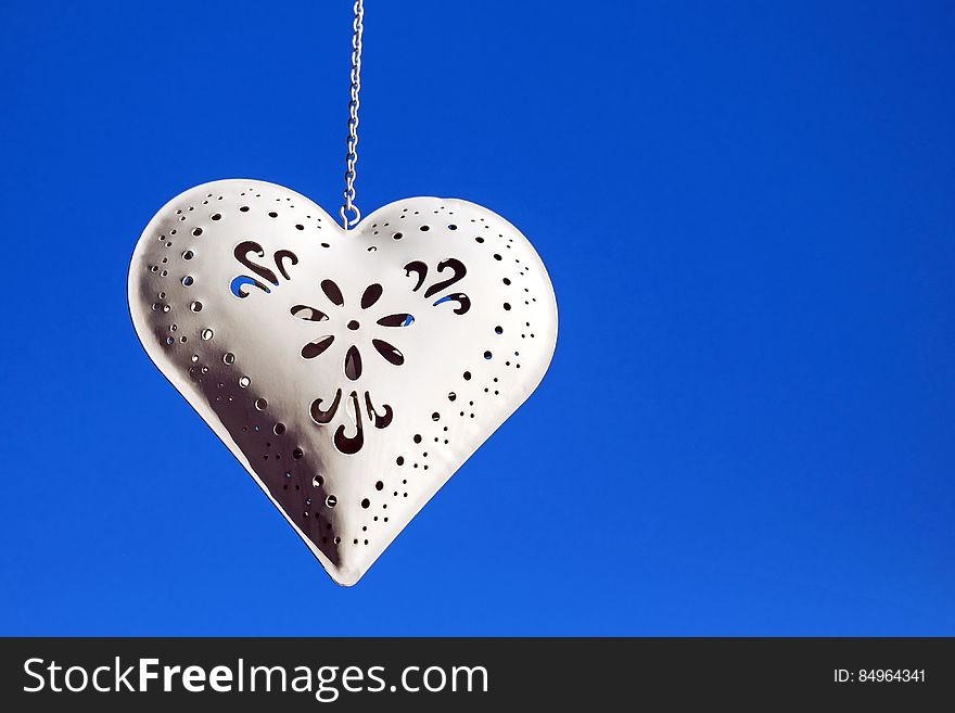A white decorative metal heart hanging from a chain.