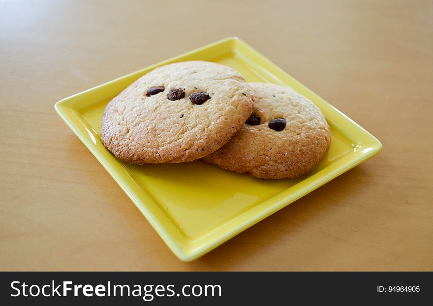 Two freshly baked chocolate chip biscuits on yellow plate.