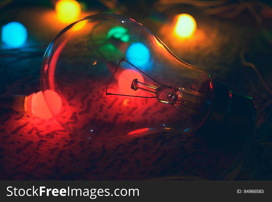 An incandescent light bulb with colorful lights in the background. An incandescent light bulb with colorful lights in the background.