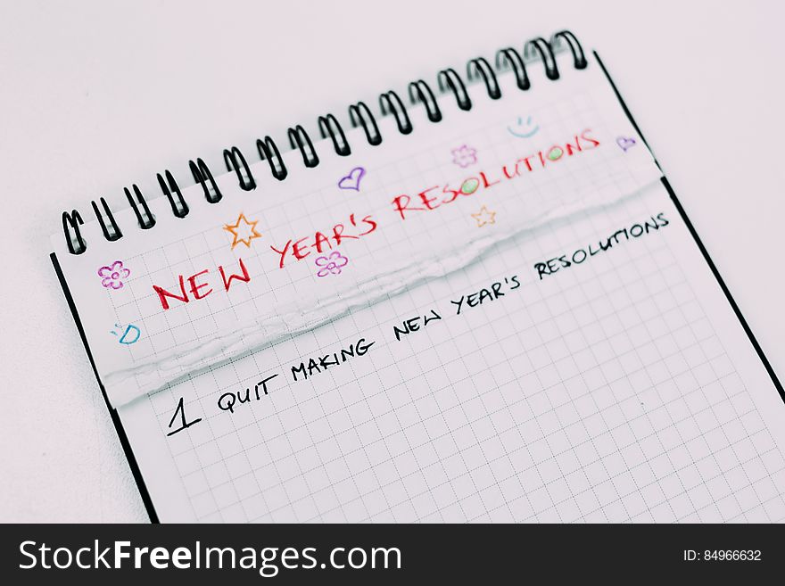 Spiral bound notebook with text at top of page in bold red uppercase letters "new years resolutions" and below it in black "1 quit making new year's resolutions".