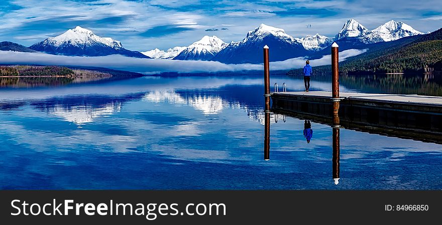 Rear view of person stood on Alpine lake pier with snow capped mountains range in background. Rear view of person stood on Alpine lake pier with snow capped mountains range in background.