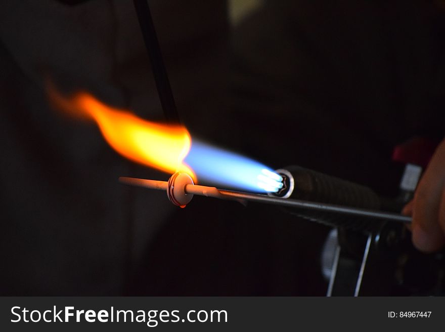 A close up of a glassworker melting a bead of glass with a blowtorch. A close up of a glassworker melting a bead of glass with a blowtorch.
