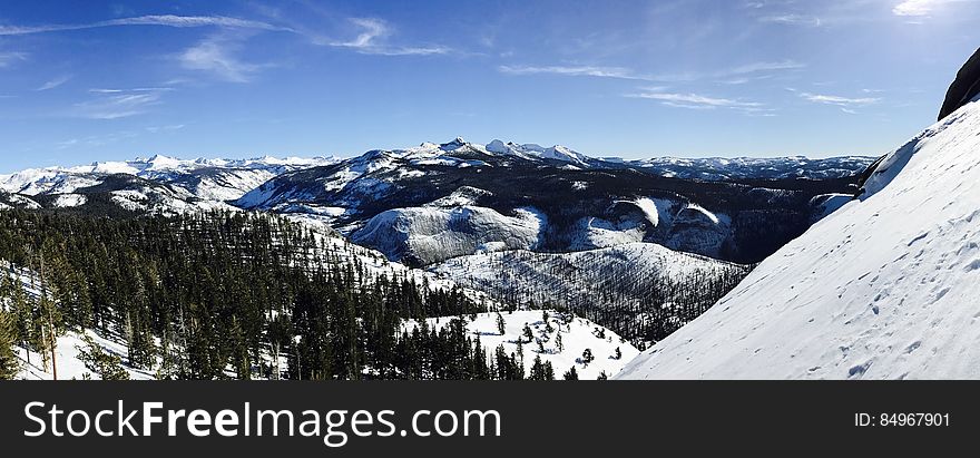 A landscape with snowy hills and forests with blue skies.
