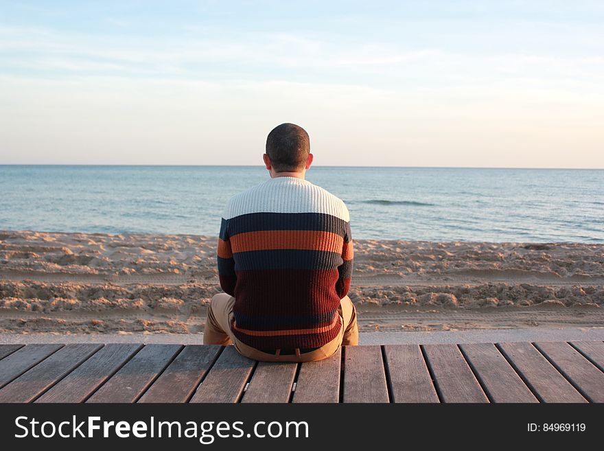 Man Sitting on Wooden Panel Facing in the Ocean