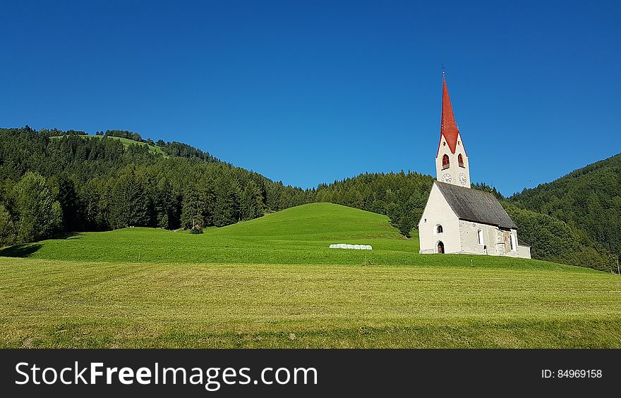 White Gray And Red Chapel On Green Field During Clear Sky Day Time