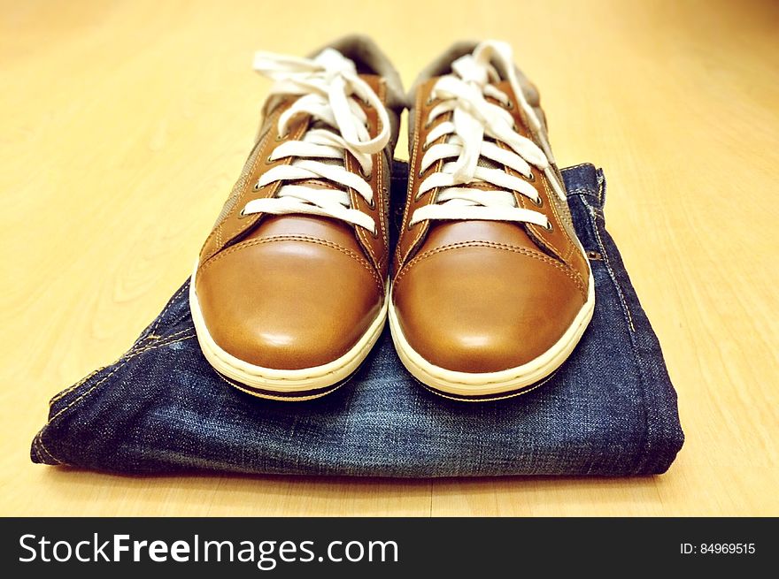 Men's brown leather shoes and jeans on a table.