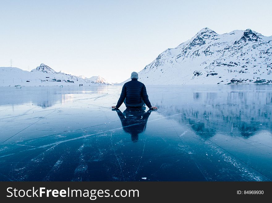 A man sitting on ice on a clear mountain lake. A man sitting on ice on a clear mountain lake.