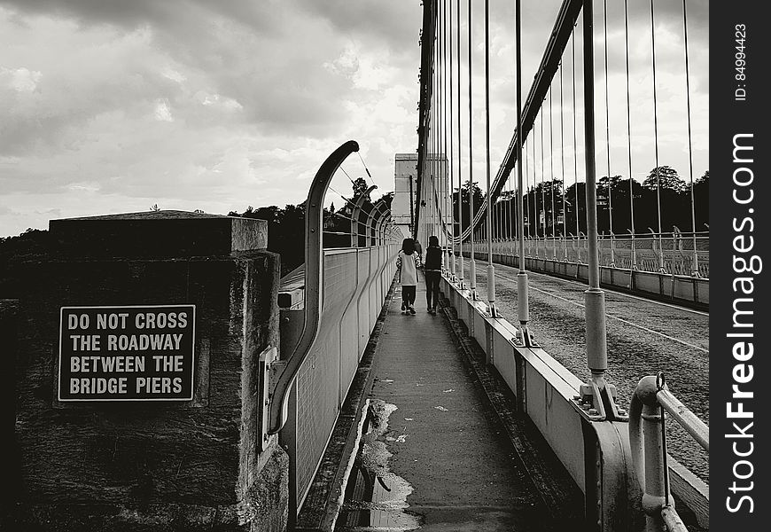 A black and white image of pedestrians crossing a bridge on a walkway next to the driveway. A black and white image of pedestrians crossing a bridge on a walkway next to the driveway.