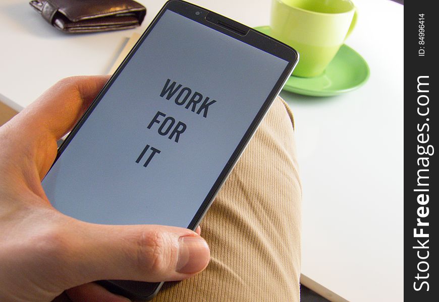 A close up of a man holding a smart phone with the text "work for it" on the screen.