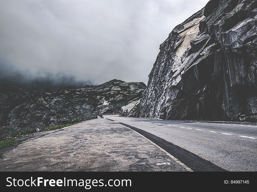 A mountain road beside cliffs in foggy weather.
