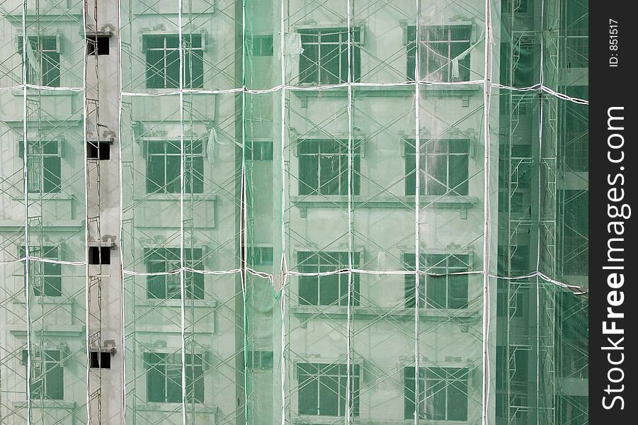 Apartment building under construction with scaffolding and green netting on its exterior. Apartment building under construction with scaffolding and green netting on its exterior.