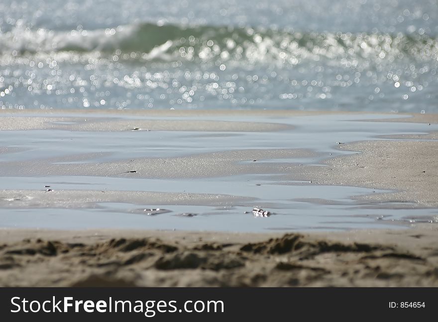 A Seashore shot which shows both sand and water. the sand in the middle is focused, and the sea-water and the close sand are blurred.