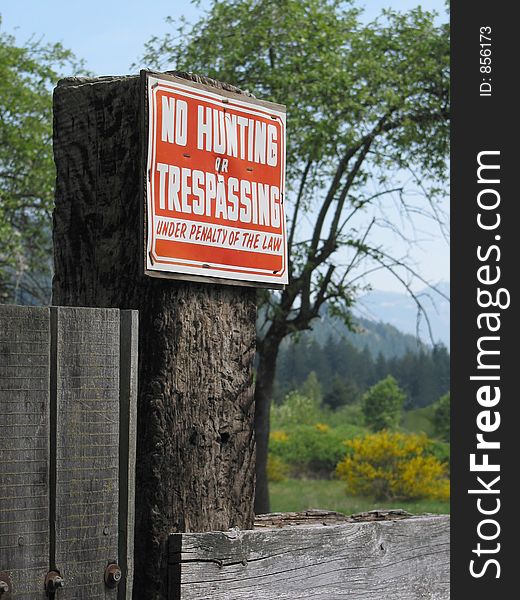 A sign warning against hunting and trespassing is attached to a fence post. A sign warning against hunting and trespassing is attached to a fence post.