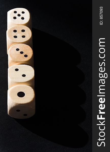 Straight row of wooden dice lit by the sun against a black background.