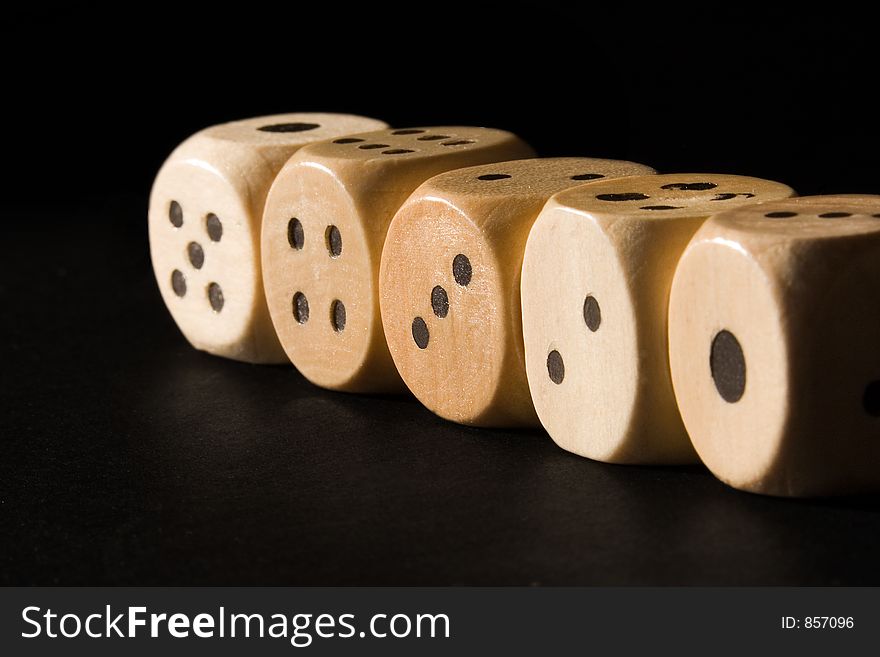 Straight row of wooden dice lit by the sun against a black background.