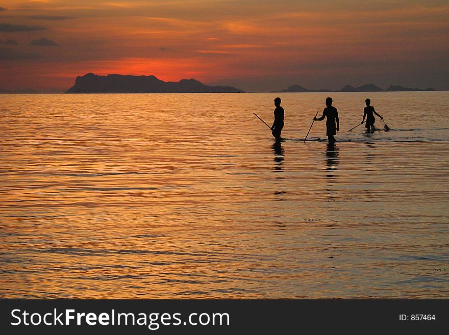 Fishermen silhouettes on vibrant tropical sunset beach