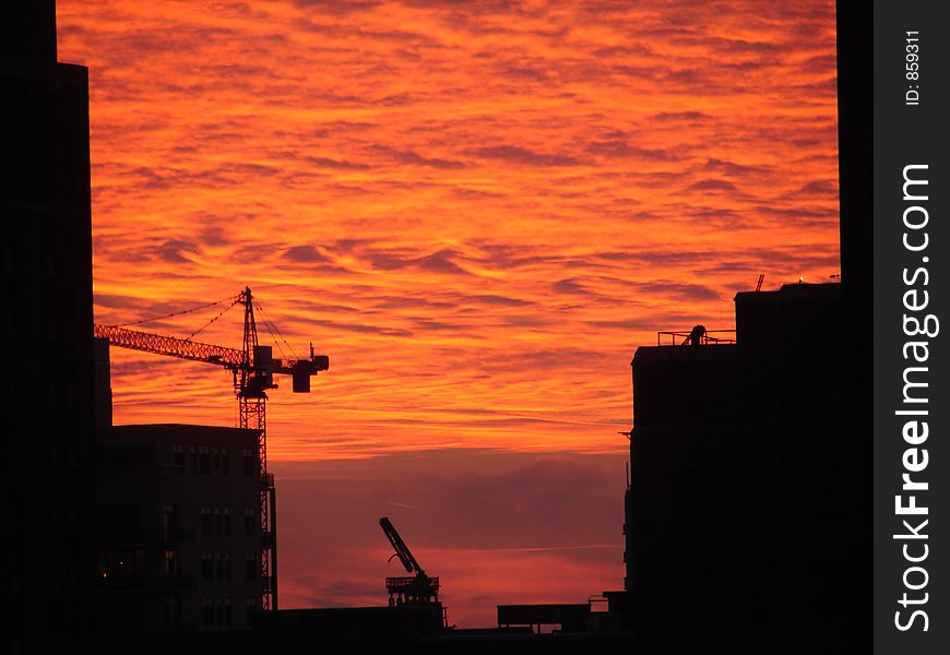 Construction cranes in Chicago building new Apartments silhouetted against a fiery sunset. Construction cranes in Chicago building new Apartments silhouetted against a fiery sunset.