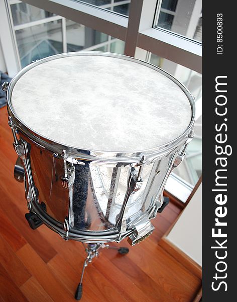 Close up of a silver snare drum against a metal, wood, and glass background. Close up of a silver snare drum against a metal, wood, and glass background.