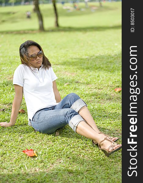 A female sitting down resting layed back and enjoying the park under a tree shade. A female sitting down resting layed back and enjoying the park under a tree shade