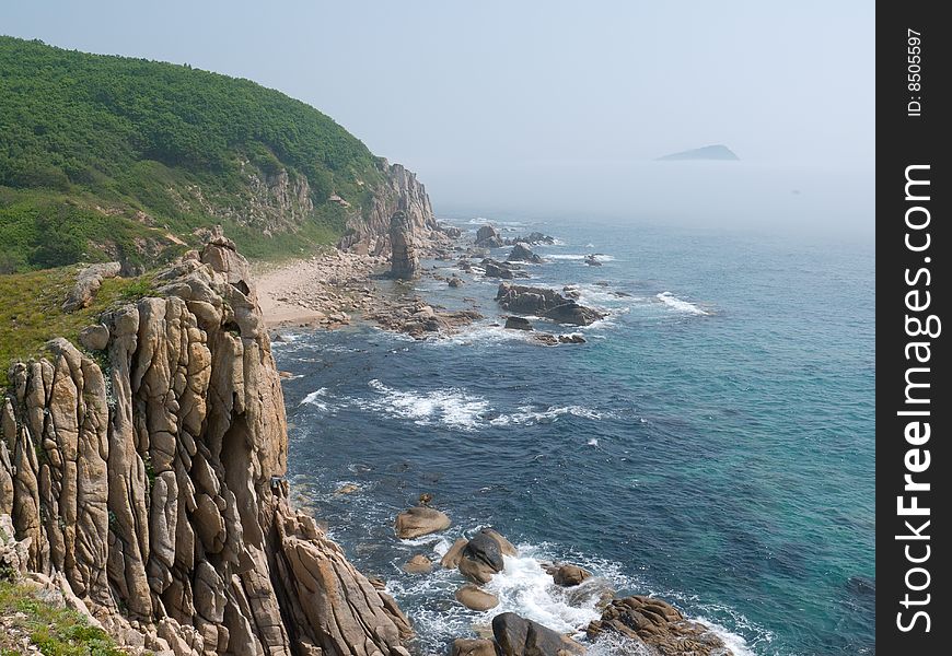 A rocky cliff on Japanese sea. On background are surf and rocks in fog. A rocky cliff on Japanese sea. On background are surf and rocks in fog.