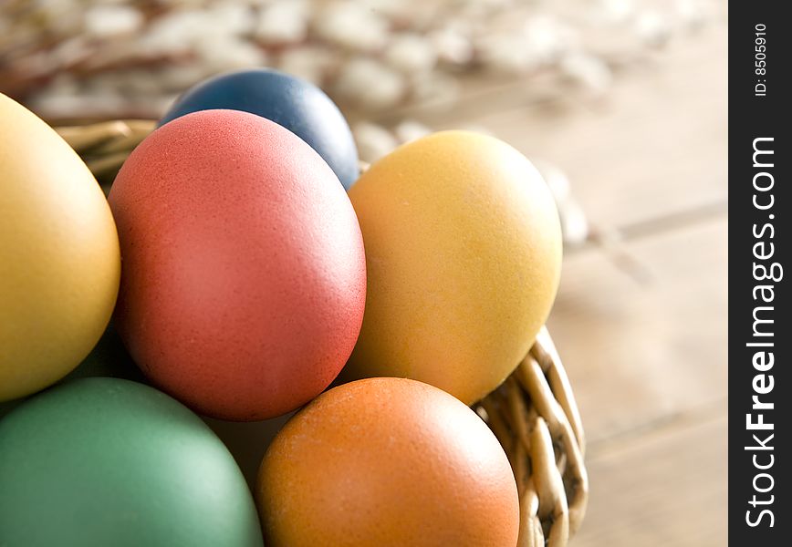 Colorful easter eggs in a basket on wooden boards. Some catkins in background.