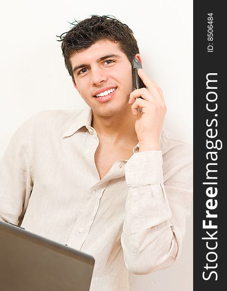 Young man in casual clothing working on his laptop while speaking at mobile phone. Young man in casual clothing working on his laptop while speaking at mobile phone