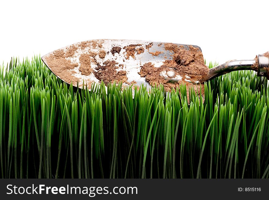 A horizontal view of a dirty garden spade on grass on a white background