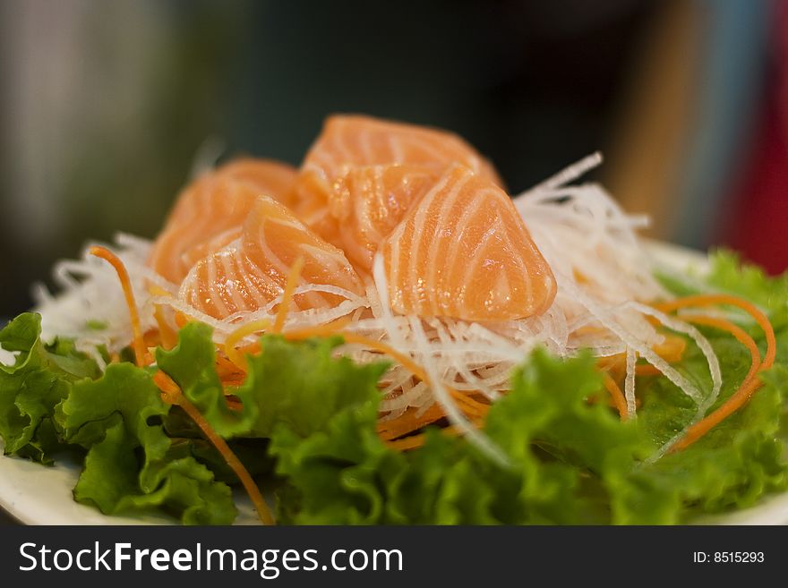 Salmon Sashimi on a plate of radish, carrota and lettuce.