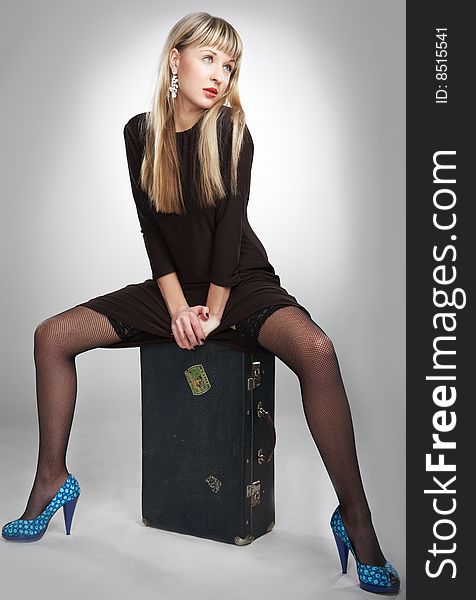 Young blonde girl with suitcase on gray background